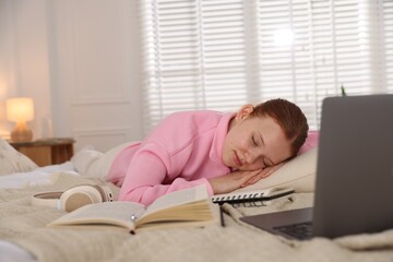 Tired teenage student sleeping near books and laptop on bed at home
