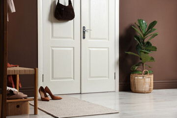 Stylish bag hanging on door and different shoes in hallway