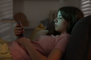 Upset teenage girl with smartphone on bed at night