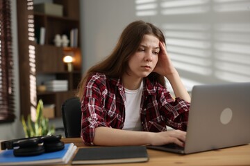 Stressed teenage girl studying at desk indoors