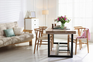 Dining table with beautiful flowers and dishware in room. Interior design