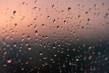 Raindrops on the window against the background of the setting sun. Background with glass and drip...