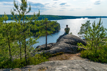 The man sitting at edge a rock and looking into the distance at the lake. The concept of reflection, loneliness, win, solitude, travel.