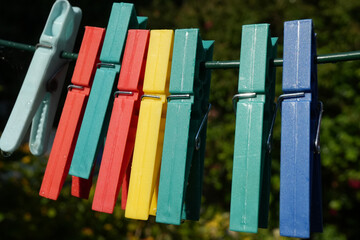 A colorful row of plastic clothespins clipped onto a clothesline in a sunny garden in England, with...