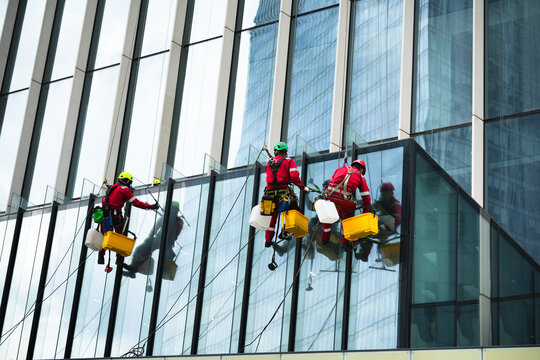 Professional window cleaners working on a glass skyscraper in full safety gear. High-risk job, urban landscape, safety protocols