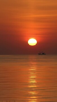 Cinematic time-lapse video of a majestic sunrise over a vast, calm ocean with sky evolving crimson to cerulean. Golden sun ascends, casting shimmering reflection on water. Distant fishing boat
