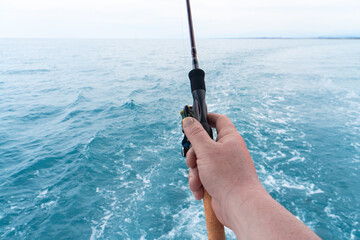 Hand of a fisherman with a spinning rod with the line on a motor boat in the sea. Fishing rod and hands of fisherman over ocean water surface.
