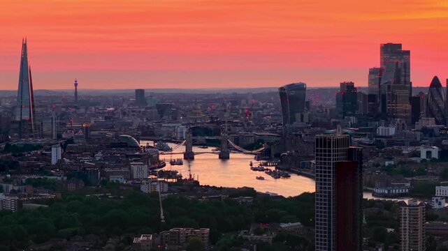 Establishing aerial view of the skyline of London, England, during a fiery sumer sunset with River Thames, Tower Bridge and city skyscrapers