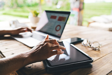 Close-up of hands multitasking on tablet and laptop with business graphs, working remotely in...