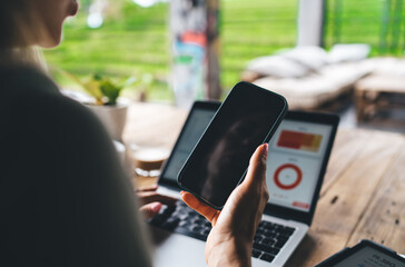 Close-up of female freelancer holding smartphone in hand, reviewing information on device while...