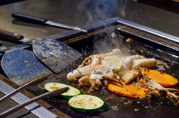 A sizzling assortment of seafood and vegetables being grilled on a hot teppanyaki plate in a...
