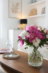 Bouquet of beautiful peonies and water on coffee table indoors. Interior design