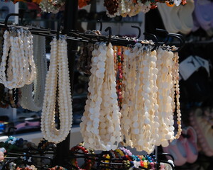 Strings of white shell beads hang on a rotating rack at an outdoor market stall, sunlit against a...