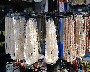 Sunlight highlights multiple layers of polished shell bead strands on a vertical jewellery rack,...