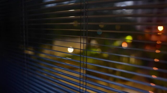 Night in apartment overlooking city street watching and hiding behind blinds. POV of detective or police or agency investigation. Suspicious and mysterious criminal activity. Looking outside