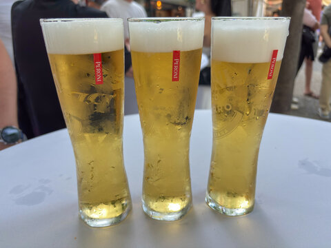 Bratislava, Slovakia, Europe - Jun 19, 2025: three glasses of peroni beer with white foam heads on a white table outdoors, concept of refreshing drinks, Italian beer, summer leisure