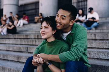 Affectionate couple sharing sweet moment sitting on historic steps, looking inspired and content while holding hands during relaxed urban adventure