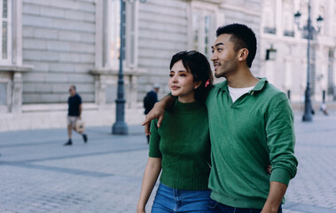 Young couple walking arm in arm on cobbled street, looking ahead with relaxed expressions. Casual moment of togetherness during urban sightseeing walk.Walking close, facing forward