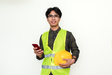 Smiling young Asian engineer confidently holds a smartphone. Isolated portrait showcasing a...
