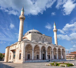 The historic Selimiye Mosque, a 16th-century Ottoman landmark in Konya, Turkey. The building features two minarets and domes, viewed from the square under a blue sky with clouds