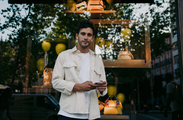 stylish young man with dark hair and light skin stands outside luxury boutique, holding...