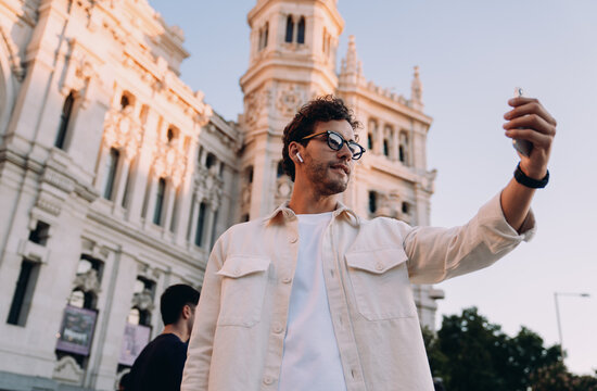 modern travel blogger films himself in front of stunning European landmark, sharing experiences in real-time. smartphone and earbuds reflect digital nomad lifestyle, blending technology and adventure