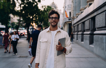 Young professional or student with a tablet smiles while walking in a lively urban setting. His confident expression reflects success, ambition, and adaptability in today’s fast-paced digital world.