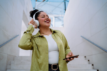 joyful woman with wireless headphones listens to music while holding a smartphone. Female enjoys a...