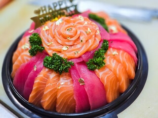 Birthday sashimi platter decorated with fresh salmon and tuna slices, arranged in a rose pattern, gold leaf flakes, parsley, and a “Happy Birthday” sign being placed by hand.