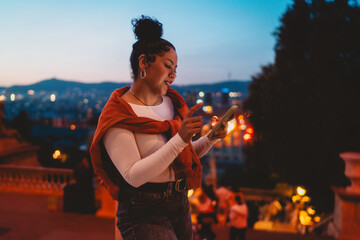 Young woman explores her smartphone at dusk, surrounded by glowing city lights. Female interacts with digital content, embracing connectivity, social media, and modern technology in urban atmosphere