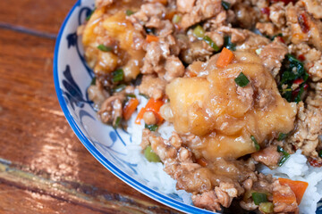 A Thai rice dish topped with stir-fried minced pork, vegetables, and battered fried egg, served in...