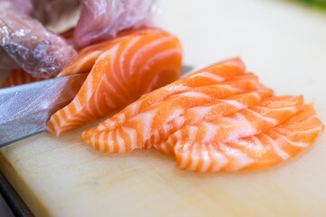 Sliced fresh salmon sashimi being prepared on a cutting board by a chef wearing gloves, showcasing the vibrant orange and white marbled texture.