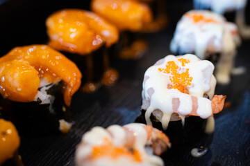 Assorted sushi topped with creamy sauces and shrimp, served on a black plate, highlighting the vibrant textures and savory presentation.