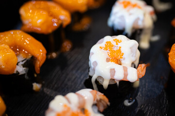Assorted sushi topped with creamy sauces and shrimp, served on a black plate, highlighting the vibrant textures and savory presentation.