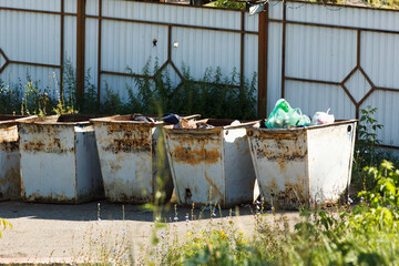 Old rusty metal garbage containers overflowing with trash. Dirty urban landscape, environmental...