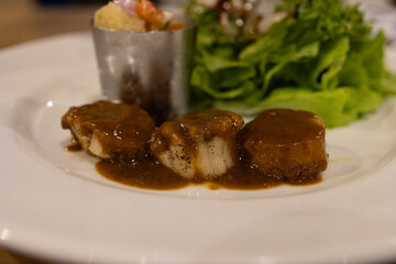 Tender beef served with rich sauce and fresh greens on a white plate.