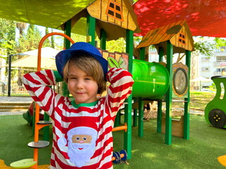 Little preschool boy in Santa Claus costume on playground, in kindergarten at resort. Christmas in...