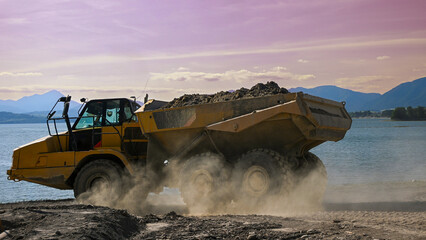 Yellow articulated hauler truck transporting earth on a construction site near a lake with...