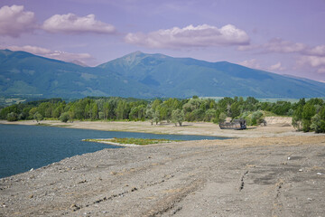 Receding water reveals abandoned ship on a dry lake bed, with mountains and cloudy sky in background