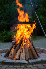 Large pile of wood is burning in a fire pit. The fire is very hot and the flames are orange. The...