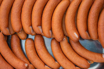 Tray of sausages stands on a table. Sausages are stacked on top of each other and are prepared for...
