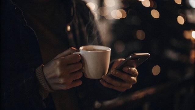 Young people are drinking hot coffee and tea beverages, holding cups and mugs in their hands at a cafe table during a business office breakfast break
