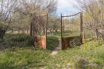 Rustic, partly cloudy scene with two gates and a dirt path leading into a wooded area Vegetation...