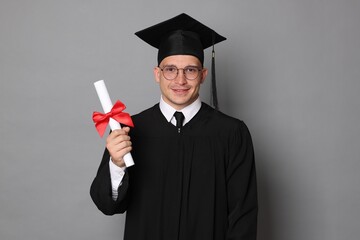 Happy student with diploma after graduation on grey background