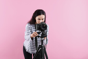 Woman with professional video camera on pink background, space for text