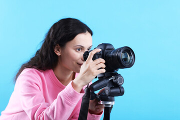 Woman with professional video camera on light blue background, space for text