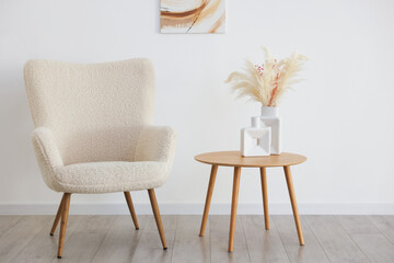 Comfortable armchair and table with vases near beige wall indoors. Interior design