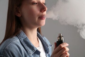 Woman using electronic smoking device on grey background