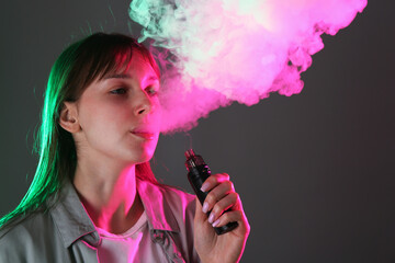 Woman using electronic smoking device in neon lights on grey background, space for text