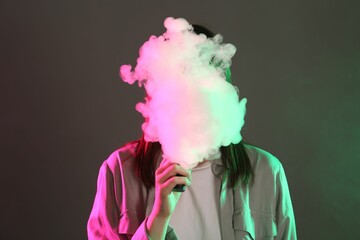 Woman using electronic smoking device in neon lights on grey background